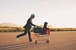 Zwei junge Geschäftsleute mit Helmen, Schutzbrille und in Business-Anzügen gekleidet fahren ihren raketengetriebenen Einkaufswagen