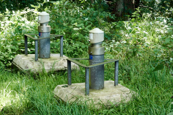 Betonierte Brunnenköpfe von Grundwasserüberwachungsbrunnen mit Stahlkollisionsschutz in einem Wald